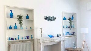Une pièce avec deux étagères blanches remplies de vases bleus, une cheminée, une petite table avec une lampe et un radiateur.