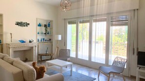 Un salon comprenant un canapé, une table basse, un chien, une cheminée, un téléviseur et une grande fenêtre avec des stores.