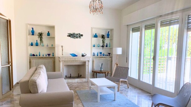 Un salon comprenant un canapé, un fauteuil, une table basse, une cheminée et des étagères ornées d’objets décoratifs.