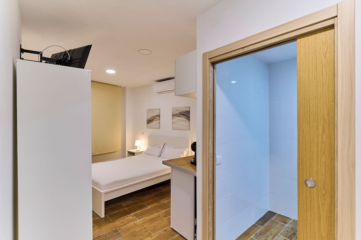 A compact room with a bed, bedside table, and a wooden door leading to a bathroom.