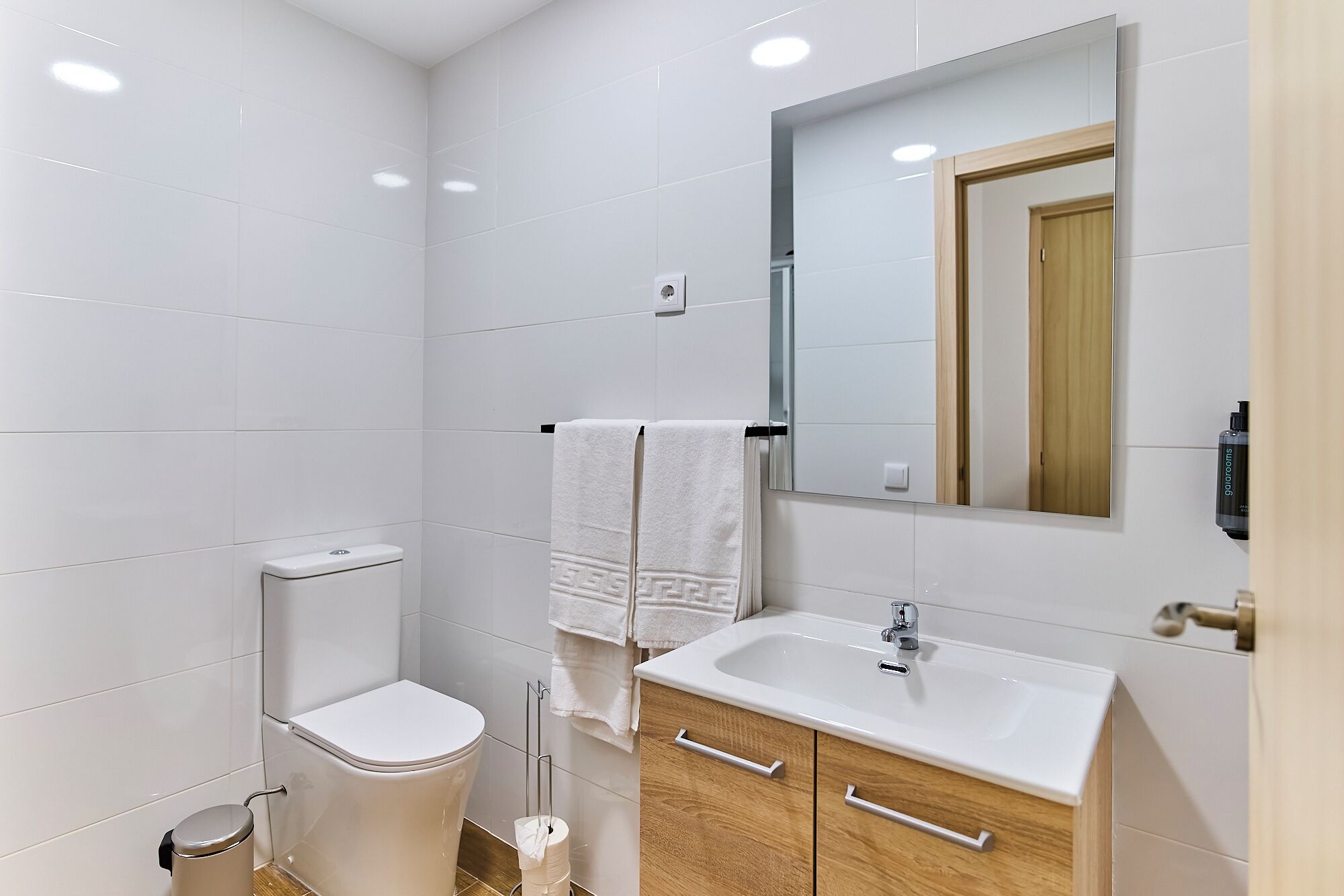 A modern bathroom with white tiles, a toilet, a sink, and a mirror.