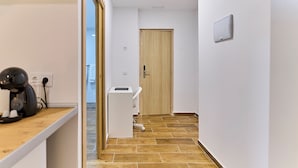 Um corredor com porta de madeira, parede branca e um pequeno balcão branco com um aparelho.