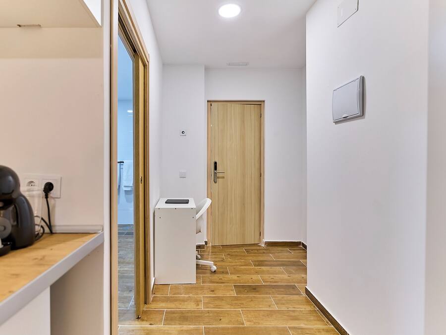 A hallway with a wooden door, a white wall, and a small white counter with a device on it.