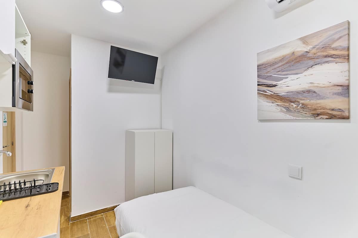 A room with a bed, a mounted TV, a painting, and a wooden cabinet.
