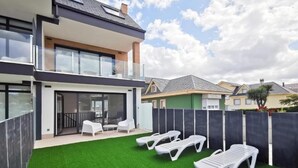 A modern two-story house with a balcony, a small patio with lounge chairs, and a well-maintained lawn. - Apartamentos Costa de Foz by gaiarooms  (Foz)