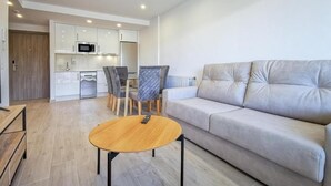 A modern living room with a sofa, a round coffee table, and a dining area with chairs and a table. - Apartamentos Costa de Foz by gaiarooms  (Foz)
