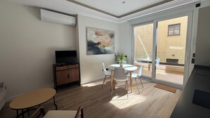 A modern living room with a flat-screen TV, a dining table with chairs, a sofa, and a sliding glass door leading to an outdoor patio. - Apartamentos Prior by gaiarooms (Salamanca)