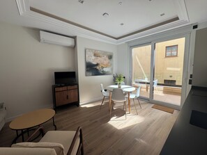 A modern living room with a flat-screen TV, a dining table with chairs, a sofa, and a sliding glass door leading to an outdoor patio. - Apartamentos Prior by gaiarooms  (Salamanca)