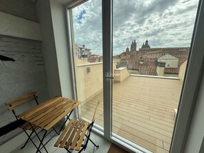 A balcony with a wooden bench, a glass door, and a view of historic buildings. - Apartamentos Prior by gaiarooms  (Salamanca)