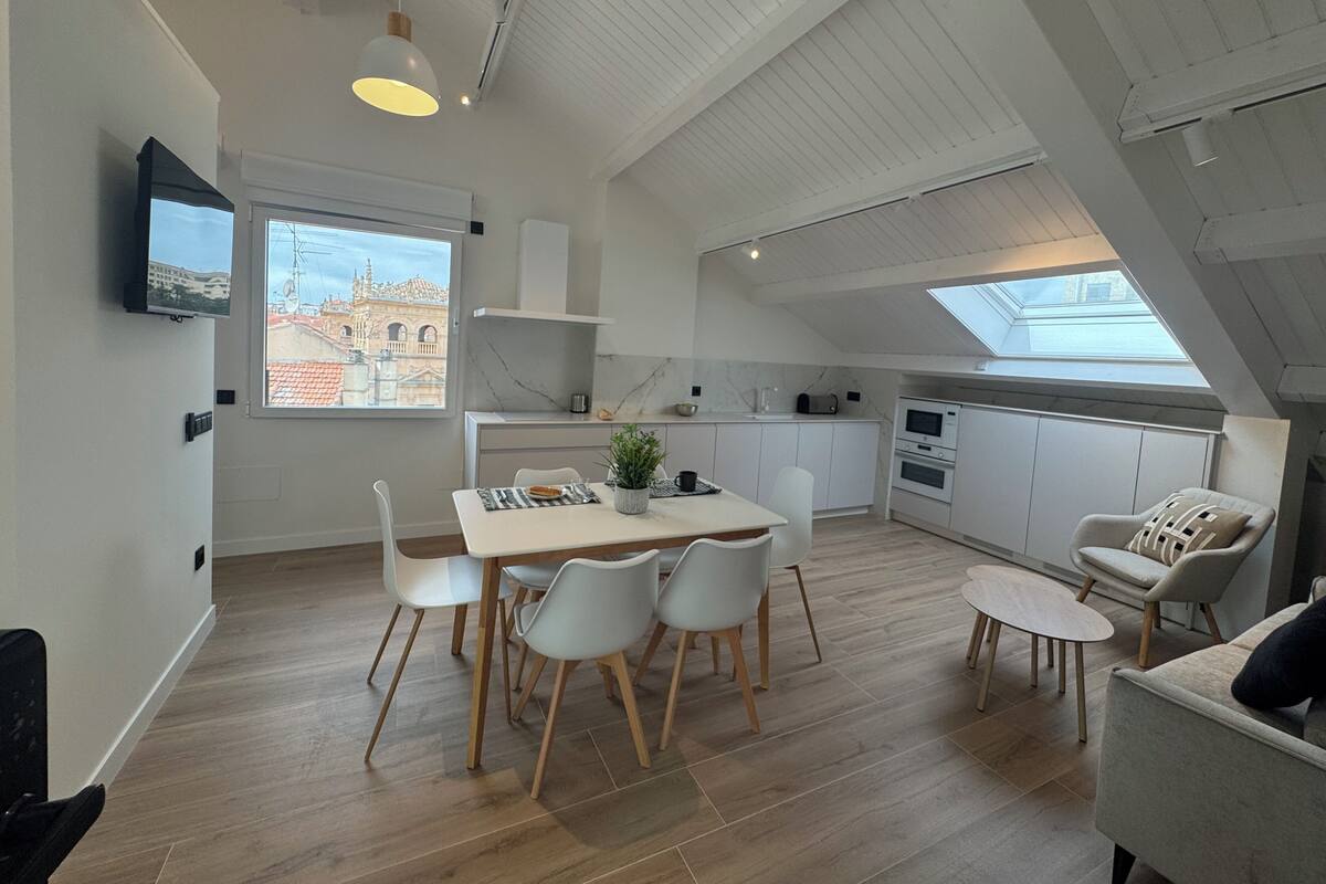 Une cuisine moderne avec des meubles blancs, un coin repas comprenant une table et des chaises, et un petit espace détente avec un canapé et un fauteuil.