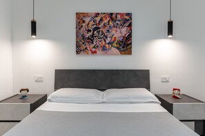 Quarto moderno com uma cama grande, duas mesas de cabeceira, um quadro abstrato colorido e luminárias pendentes.