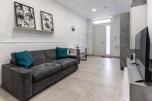 Uma sala de estar moderna com um sofá cinza, almofadas verde-água, uma TV de tela plana e arte abstrata na parede.