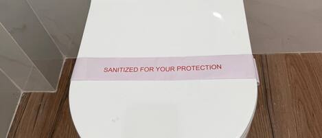 A white toilet with a black and white tiled wall and a pink sanitization tape.