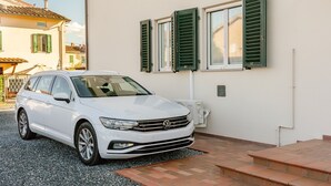 Ein weißes Auto vor einem Gebäude mit grünen Fensterläden, einer weißen Wand und einem Ziegeldach.