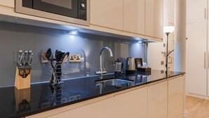 Una cocina moderna con encimera negra, pileta de acero inoxidable y cafetera.