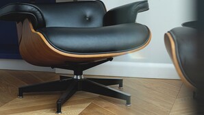 A modern office chair with a wooden frame and black upholstery, positioned on a wooden floor with a blue bookshelf in the background. - RentPlanet - Piotrkowska (Łódź)
