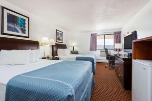 Une chambre d’hôtel avec deux lits, un bureau avec un ordinateur, une télévision et une fenêtre avec des rideaux.