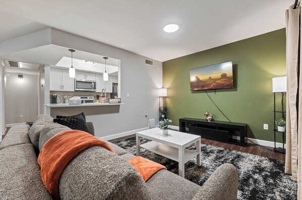 A modern living room with a grey sofa, a white coffee table, a black entertainment unit, and a green accent wall.