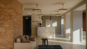 A reception area with a stone counter, a sofa, a dark ottoman, and hanging pendant lights. - Hotel Meteo Kakheti (Telavi)