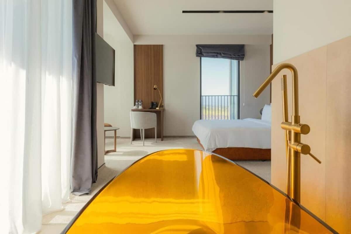 Una habitación de hotel con una cama, un escritorio, una silla, un televisor y un ventanal grande.
