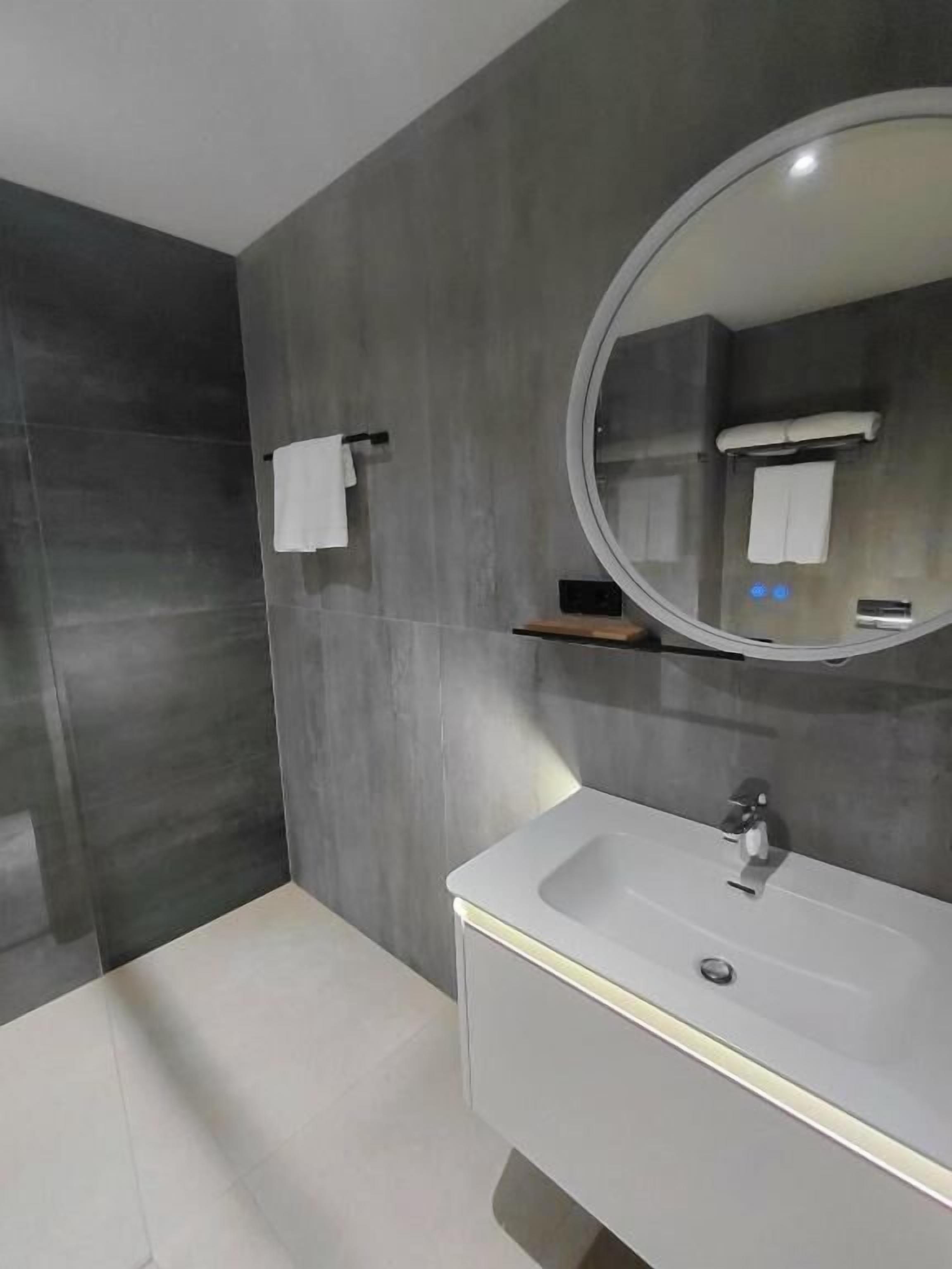 A modern bathroom with a large mirror, a white sink, and a towel rack.