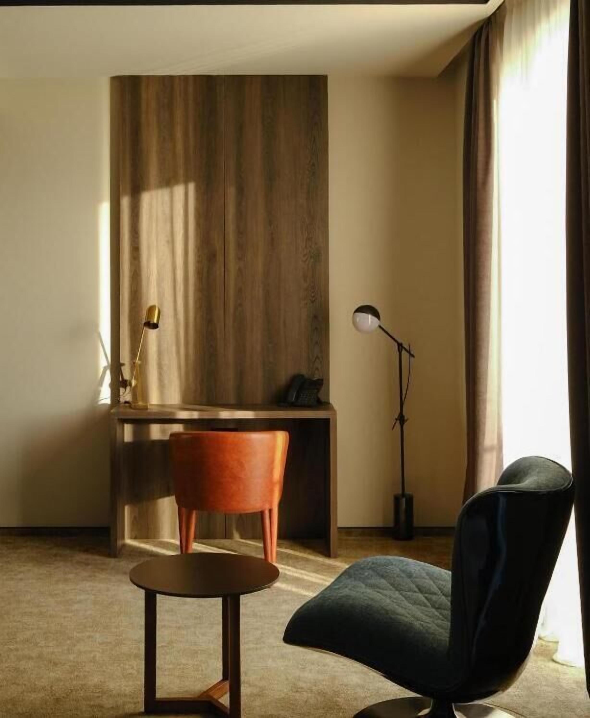 Una habitación moderna con escritorio, una silla, lámpara de pie y un amplio ventanal con cortinas.