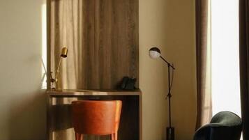 Una habitación moderna con escritorio, una silla, lámpara de pie y un amplio ventanal con cortinas.