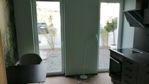 Een kamer met een eettafel, een stoel, een keukenhoek met kastjes en uitzicht door de deur.