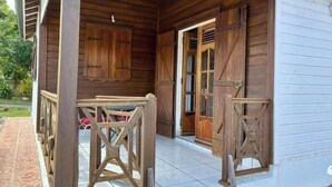 Een houten veranda met een betegelde vloer, een houten bankje en een deur naar binnen.
