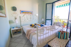 A bedroom with a bed, bedside table, lamp, and a view of the outside balcony. - Veronica's House Otranto: Sea View, Wi-Fi & Air Conditioning (Otranto)