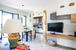 A living room with a TV, a dining area, and a kitchen in the background. - Veronica's House Otranto: Sea View, Wi-Fi & Air Conditioning (Otranto)