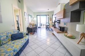 A living room with a sofa, a dining area with a table and chairs, a kitchen area with a counter and cabinets, and a staircase leading to another level. - Veronica's House Otranto: Sea View, Wi-Fi & Air Conditioning (Otranto)