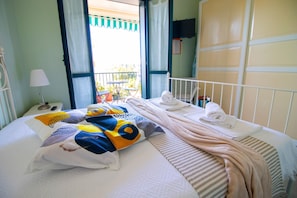Ein Hotelzimmer mit Bett, Kissen, einem Nachttisch mit Lampe, einem Babybett und Blick auf den Balkon.