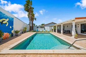 A swimming pool with lounge chairs, a covered patio area, and a mural on the wall.