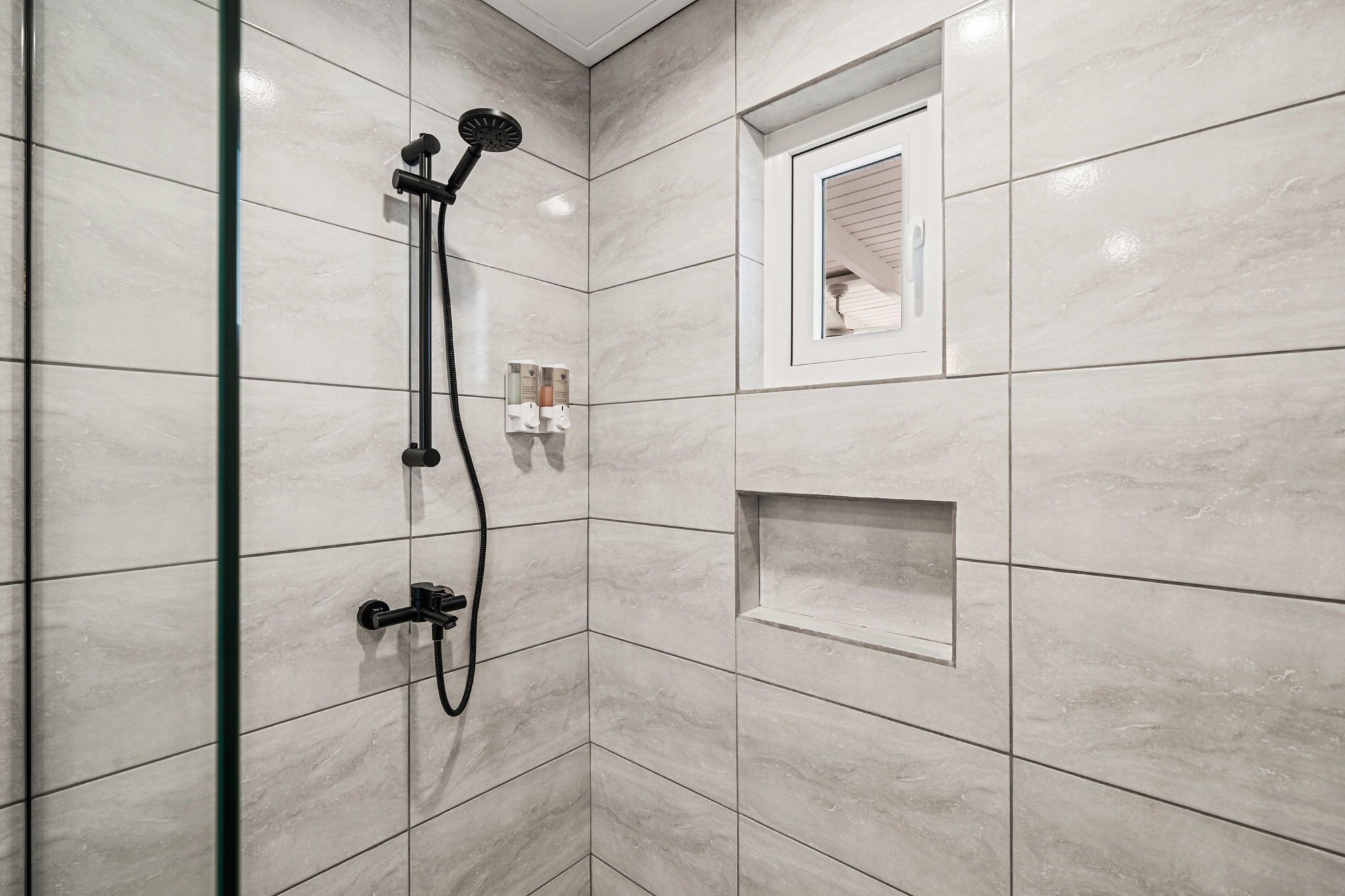 A bathroom with a shower, a mirror, and a shelf.
