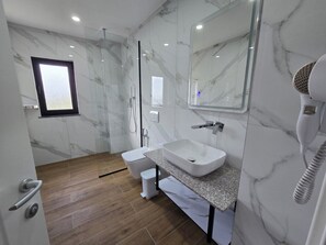 A modern bathroom with a marble wall, a built-in sink, a shower, and a hairdryer. - Vila 2M (Sarandë)