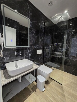 A modern bathroom with a large mirror, a white sink, a toilet, and a shower area. - Vila 2M (Sarandë)