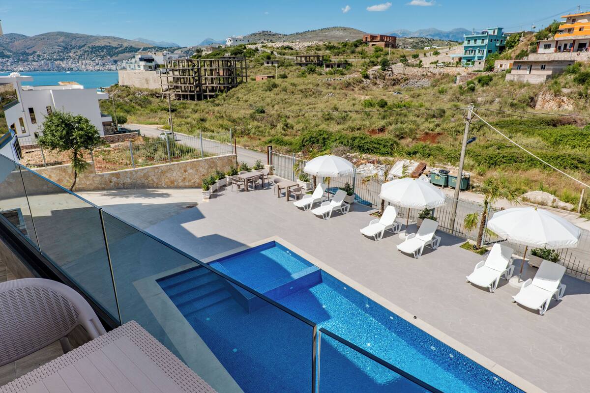 Una piscina en la azotea con sillas de descanso y sombrillas, con vistas a un paisaje urbano costero.