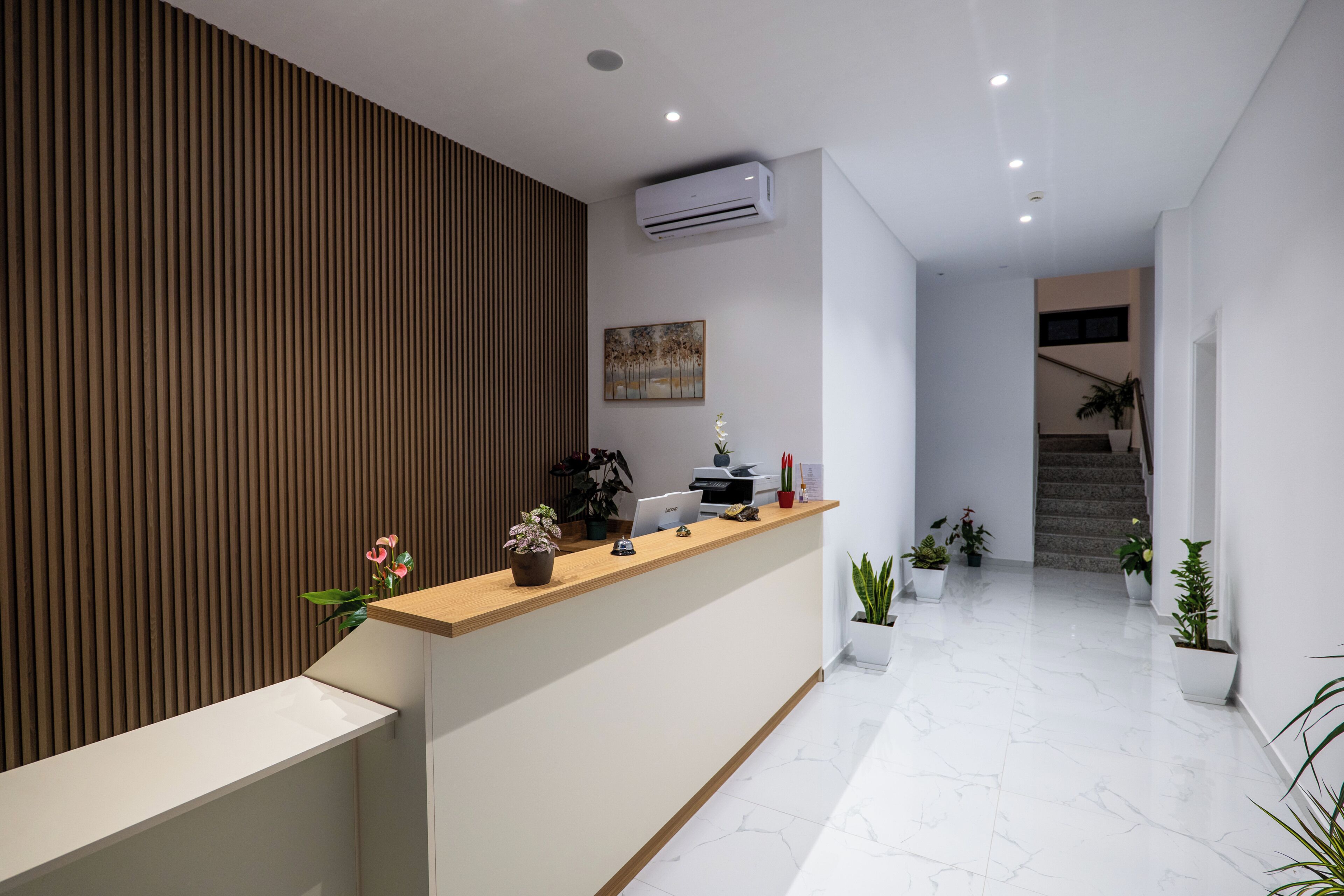 Zona de recepción con pared de paneles de madera, mostrador de recepción y plantas en macetas.