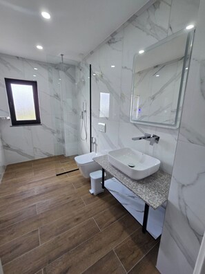 A modern bathroom with a marble wall, a large mirror, a sink, and a shower. - Vila 2M (Sarandë)