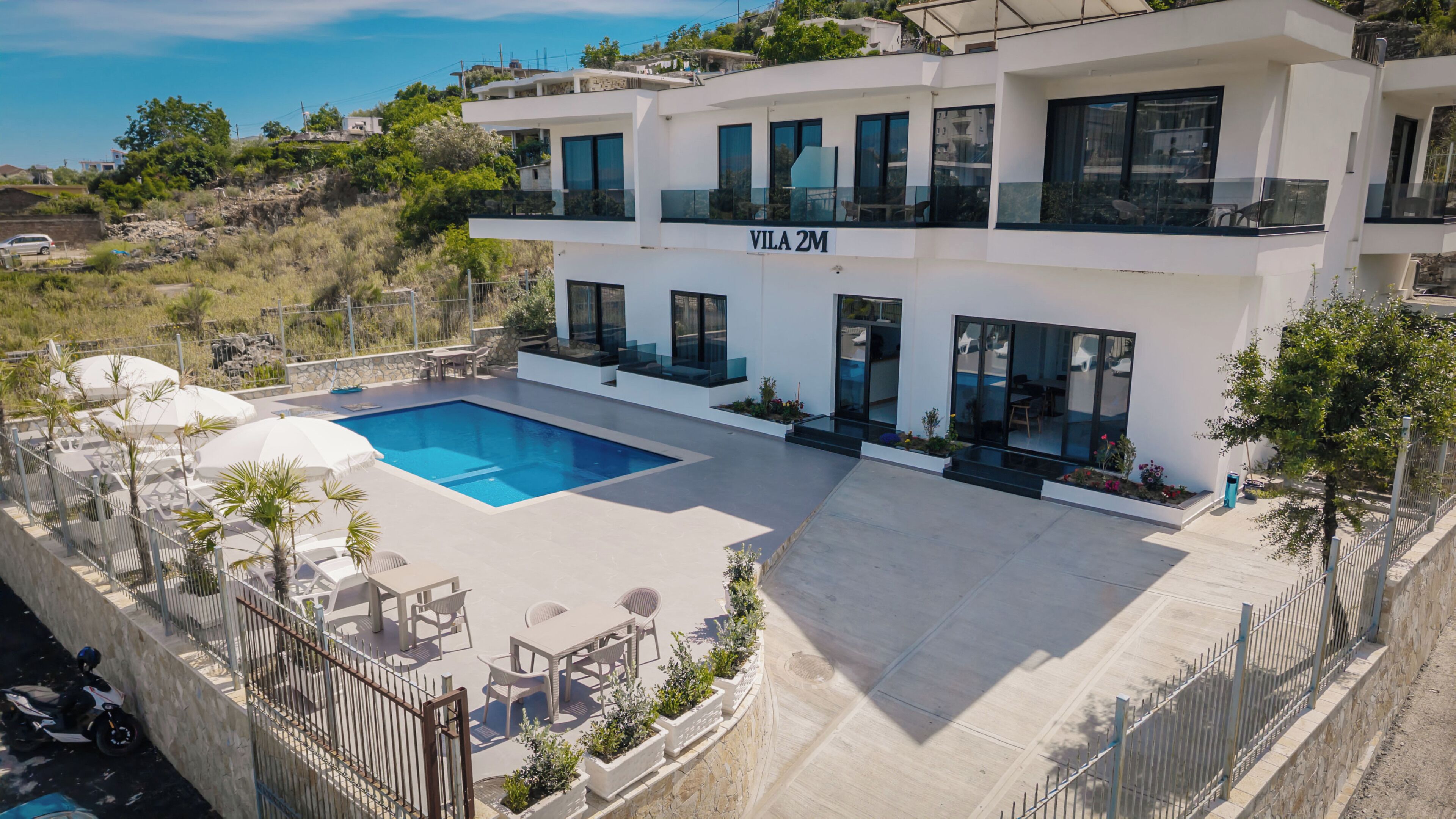 A modern villa with a swimming pool, outdoor seating, and a view of the surrounding landscape.