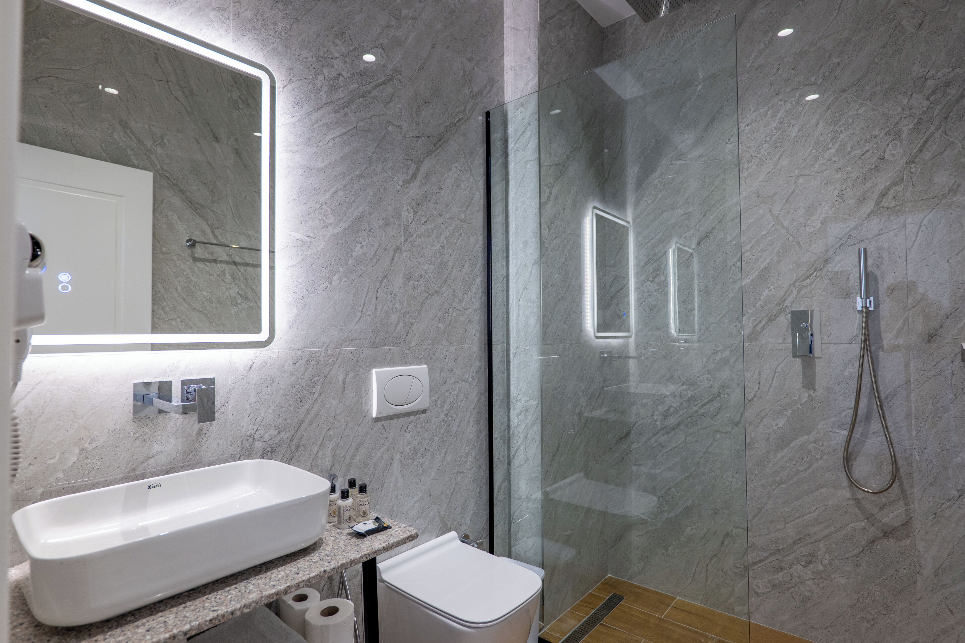 Un baño moderno con pared de mármol, cabina de ducha de vidrio, lavamanos blanco y un inodoro.