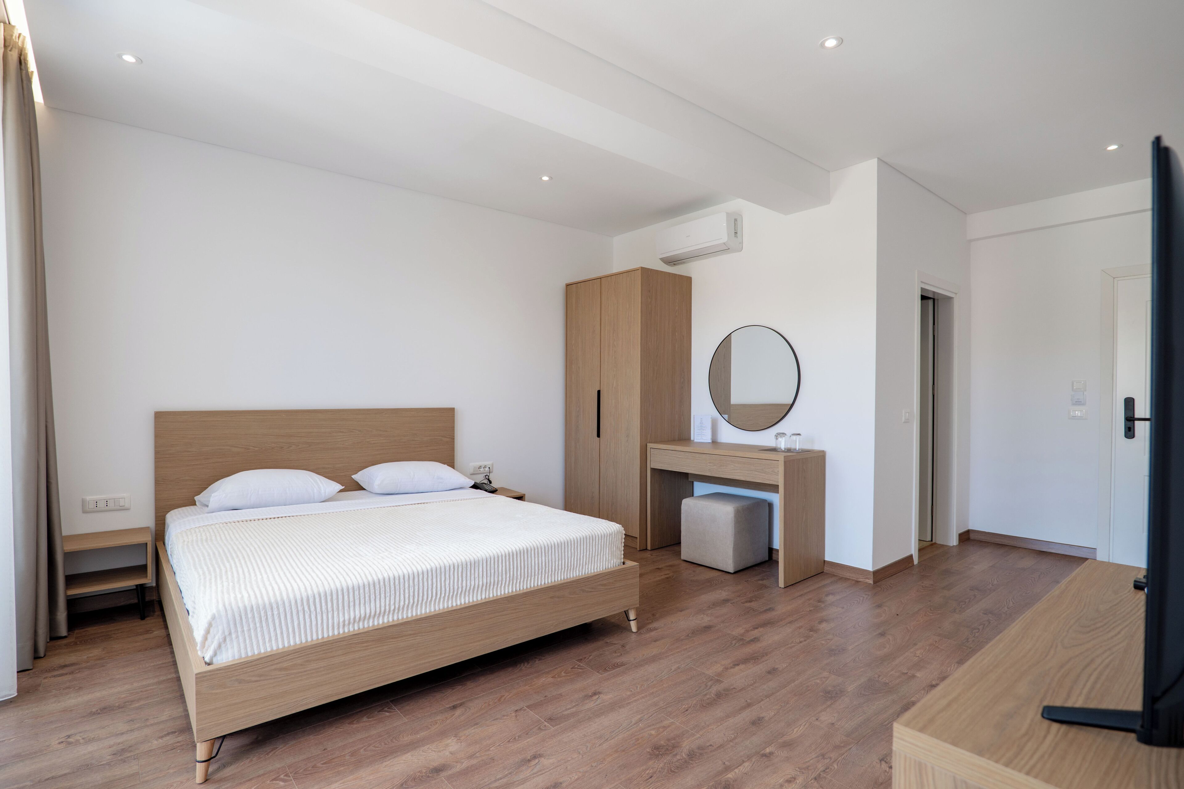 A bedroom with a wooden bed, a desk with a mirror, a wardrobe, and a television.