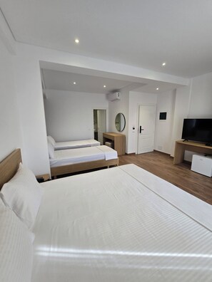 A modern hotel room with two beds, a TV, a small desk, and a door leading to another room. - Vila 2M (Sarandë)
