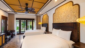 A hotel room with two beds, a ceiling fan, a wooden headboard, a desk with a chair, and a view through the glass door. - Ancient Retreat Hoi An (Da Nang)