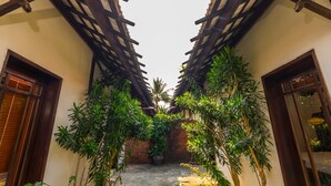 A narrow alleyway with wooden beams overhead, brick walls, and lush greenery. - Ancient Retreat Hoi An (Da Nang)