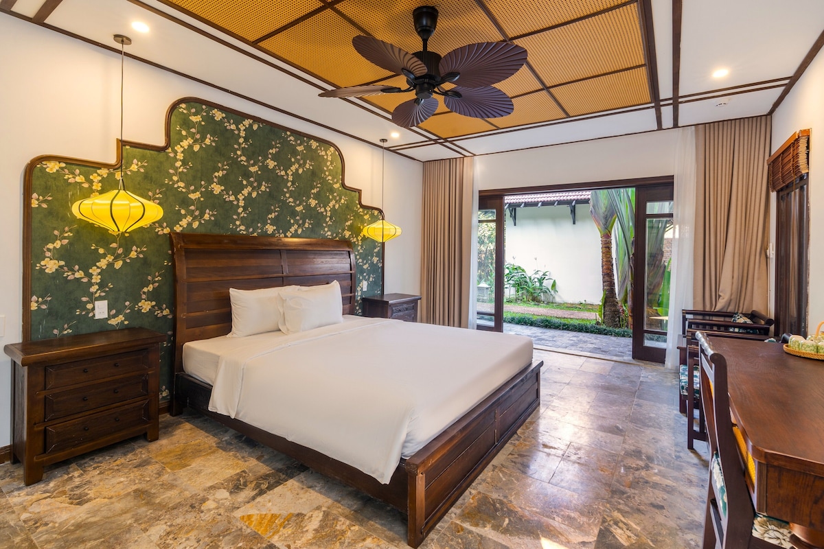 A bedroom with a large bed, wooden nightstands, a ceiling fan, and a view of the outdoors.