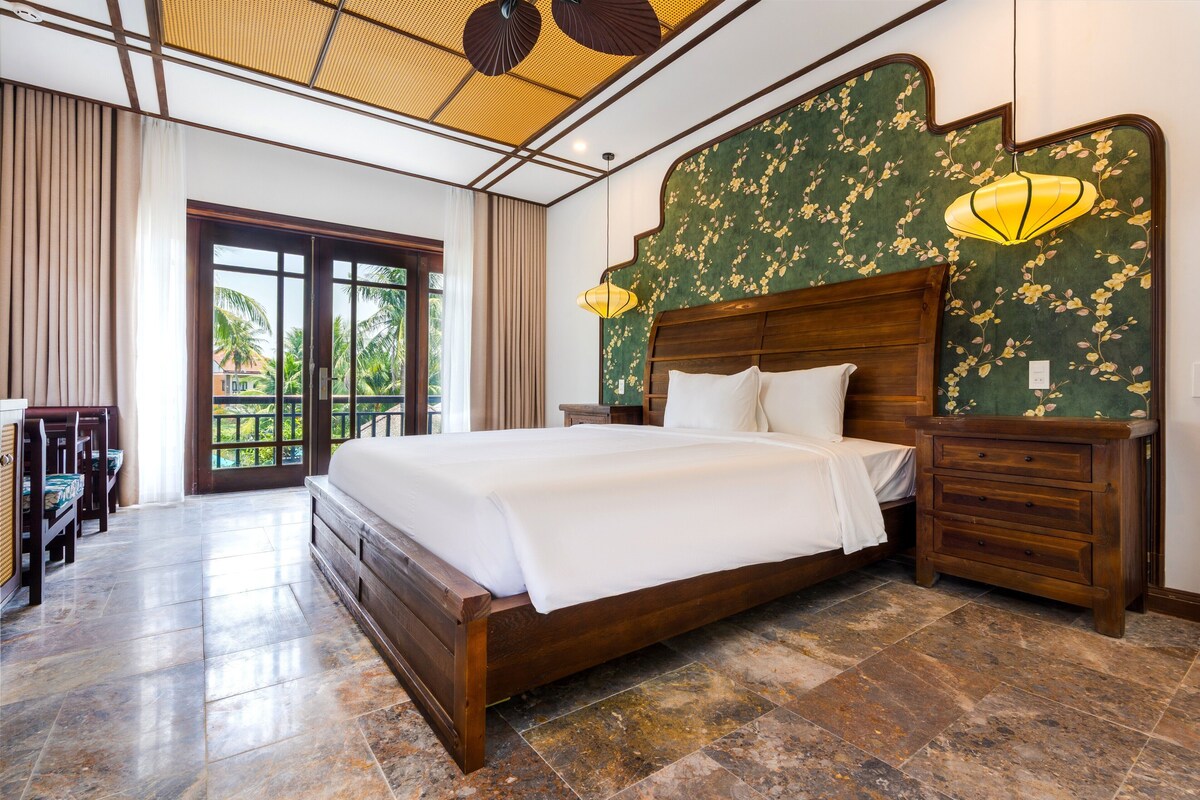 A bedroom with a large bed, wooden headboard, two bedside tables, and a view of the outdoors through a glass door.