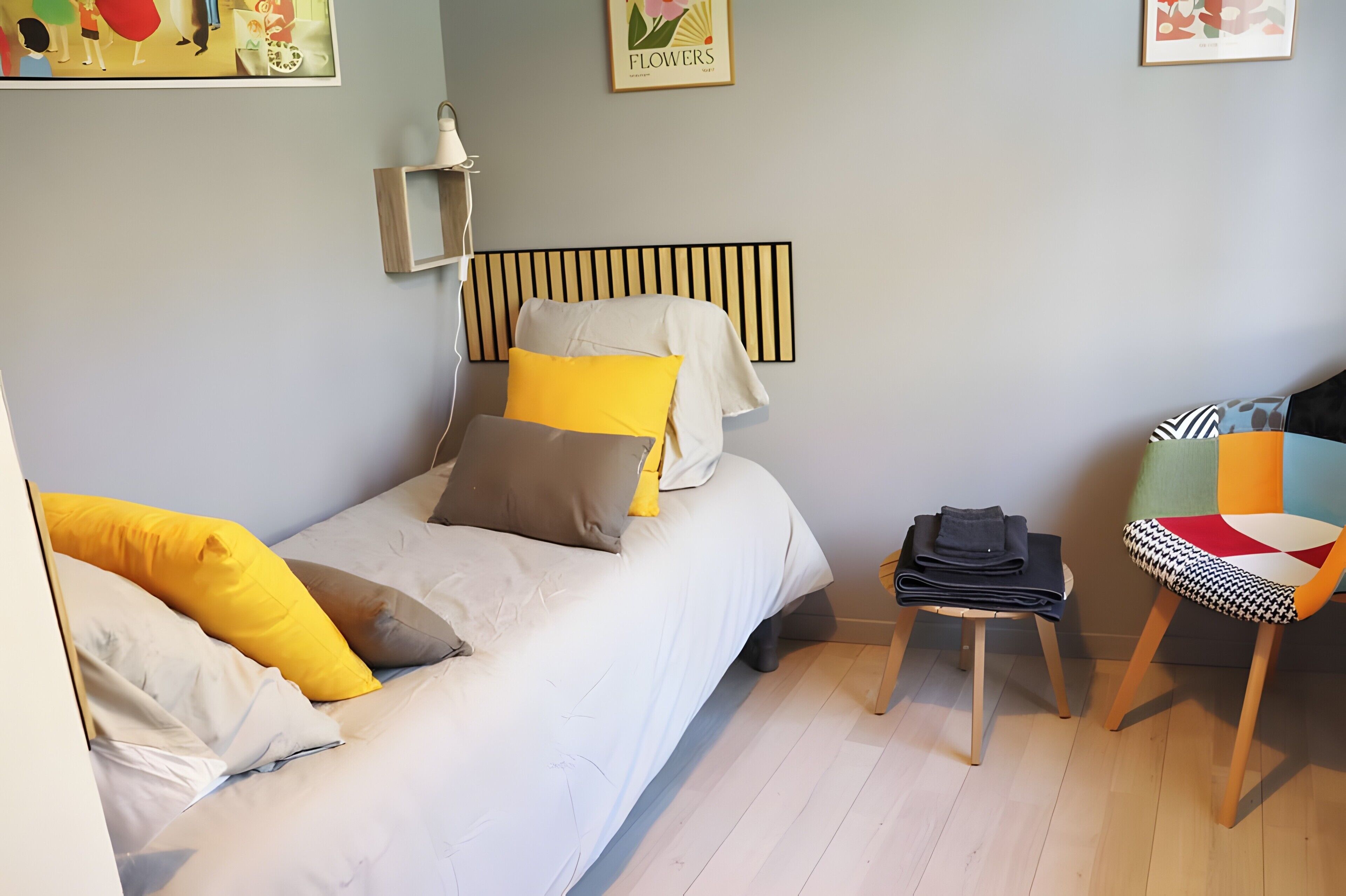 Un dormitorio con cama, almohadas, mesita de noche, silla y estante de pared.