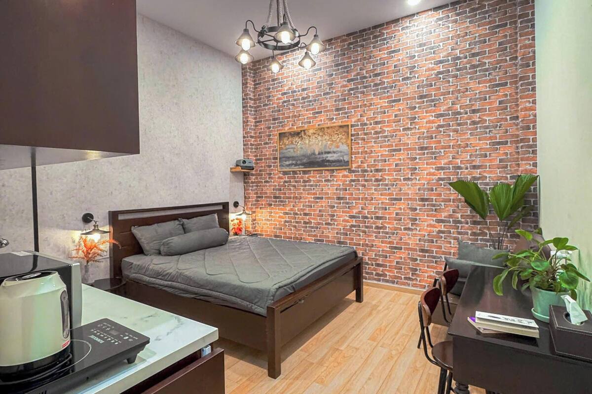 A modern bedroom with a brick wall, a bed, a desk, and a coffee maker.